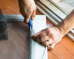 person using boxcutter to repair window screen