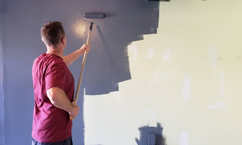 man painting a purple accent wall with long handled roller brush